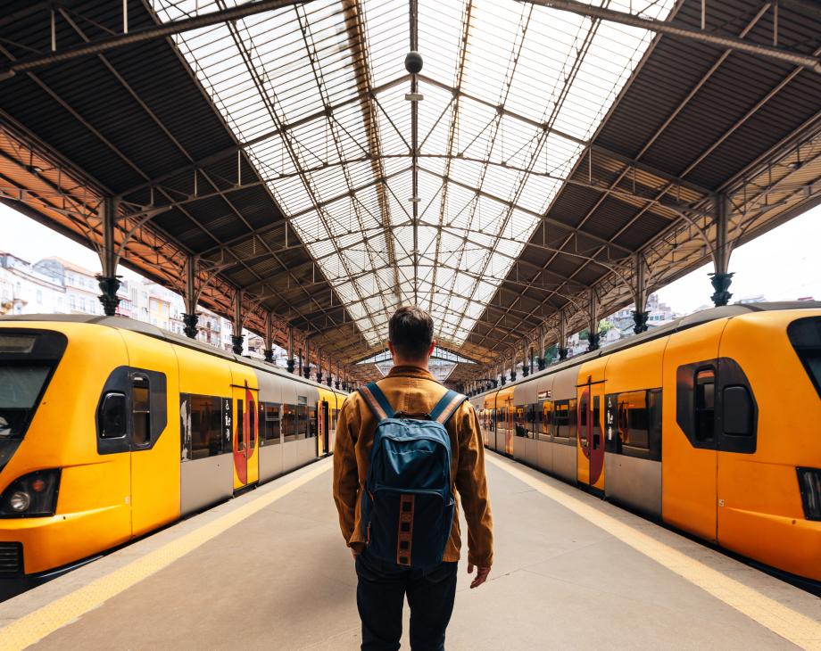 Color photo of man with backpack at a train station facing two trains